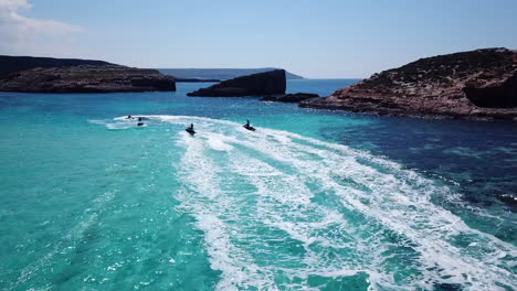 Drone-following-men-on-jet-skis-in-crsytal-clear,-turquoise-water-on-comino-island-in-malta