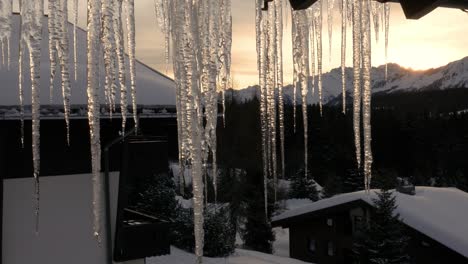 Schmelzende-Eiszapfen-Bei-Sonnenaufgang-Vor-Der-Kulisse-Schneebedeckter-Berge-Und-Wälder