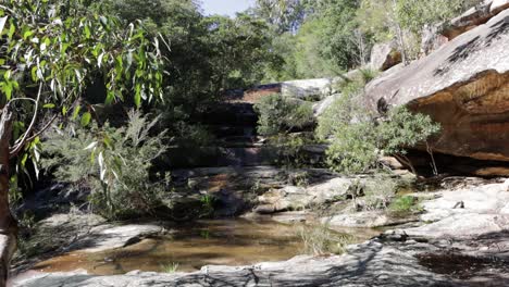 Somersby-falls-in-the-Brisbane-Water-National-Park-with-a-woman-walking-over-the-rock-ledge,-Locked-wide-shot