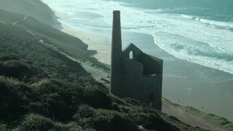 Cornish-tin-mine-pump-house-on-the-north-Cornwall-coast-with-people-walking-the-coastal-paths-and-the-beach