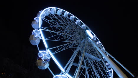 Weiß-Beleuchtetes-Riesenrad-Als-Attraktion-Für-Besucher-Des-Weihnachtsmarkts-In-Brünn-Auf-Dem-Moravske-Namesti,-Das-Passagiere-Hoch-Hinauf-Befördert,-Um-Einen-Blick-Auf-Die-Stände-Bei-Nacht-Zu-Ermöglichen,-Aufgenommen-In-4K-60fps-Zeitlupe