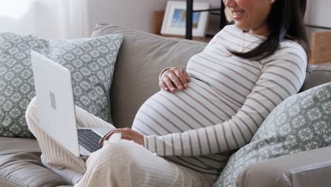 Feliz-Mujer-Asiática-Embarazada-Con-Computadora-Portátil-En-Casa.-Concepto-De-Embarazo,-Descanso,-Personas-Y-Expectativas-Feliz-Sonriente-Mujer-Asiática-Embarazada-Con-Computadora-Portátil-Sentada-En-Un-Sofá-En-Casa