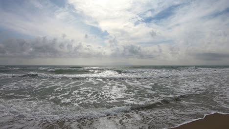 Sand-beach-with-sea-waves-and-foams,-blue-sky-with-white-clouds,-slow-motion-footage,-centered-view