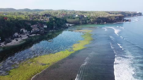 Toma-Aérea-Que-Se-Eleva-Sobre-Un-Espejo-De-Vidrio-Como-El-Agua-Separada-Por-Un-Arrecife-Verde-En-Padang,-Bali