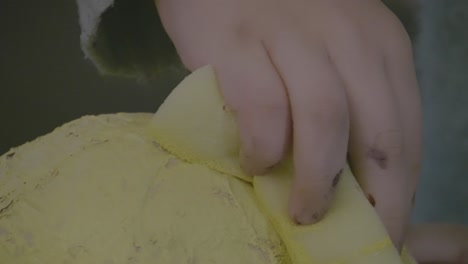 A-close-up-macro-shot-of-a-girl-sponge-painting-some-yellow-paint-onto-some-paper-mache-crafts