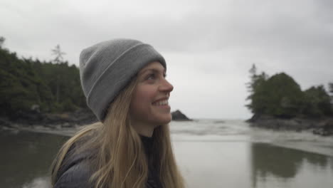 Close-up-of-a-girl-smiling-and-walking-on-the-beach-in-Tofino-British-Columbia-Canada-on-a-cloudy-morning-with-waves-coming-in-on-the-sand