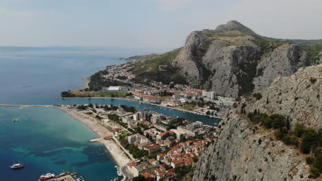 Hazy-sunny-summer-day-aerial-panoramic-footage-over-Omis-town,-river-Cetina-and-cliffs