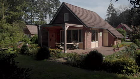 Slow-aerial-distancing-showing-a-summerhouse-in-The-Netherlands-with-garden-roof-and-terrace-in-natural-and-green-surrounding-in-a-recreational-park-against-a-blue-sky