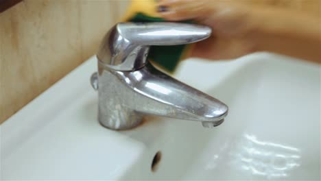 Woman-cleaning-water-faucet-with-sponge