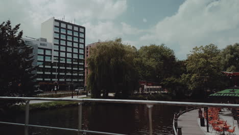 Slow-motion-shot-crossing-over-a-bridge-with-views-of-a-canal-and-buildings,-people-in-the-foreground