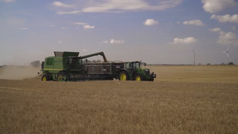 Una-Cosechadora-Verde-Está-Cosechando-Un-Campo-De-Trigo-Y-Al-Mismo-Tiempo-Descargando-La-Carga-Sobre-El-Carro-Que-Está-A-Su-Lado.