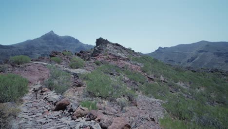 Female-hiker-in-the-distance-walking-on-a-rocky-path-with-mountains-in-the-background-in-Teno-mountains,-Tenerife