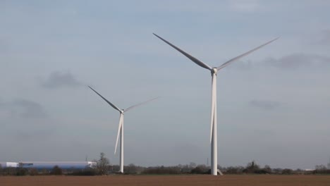 A-pair-of-slowly-spinning-wind-turbine-in-the-middle-of-a-brown-field