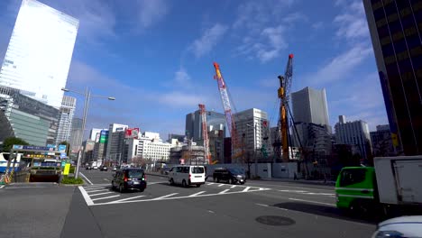 Calle-Muy-Transitada-Con-Coches-Pasando-En-Tokio,-Japón,-Con-Un-Sitio-De-Construcción-Al-Fondo