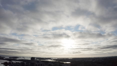 Vista-Aérea-Inclinada-Hacia-Arriba-De-La-Ciudad-Costera-Y-La-Puesta-De-Sol-Detrás-De-Las-Nubes