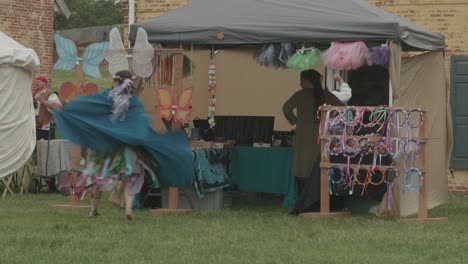 Merchandise-vendor-dances-by-her-stall-foreground-at-a-renaissance-fair,-Philadelphia-Renaissance-Fair,-Fort-Mifflin,-Pennsylvania