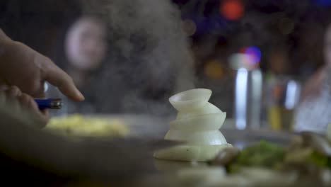 Onion-volcano-getting-lit-by-Teppanyaki-chef-during-dining-experience,-slowmo-HD