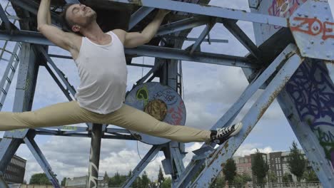 Graceful-male-dancer-performing-splits-on-metal-crane-while-reaching-to-camera-with-hand