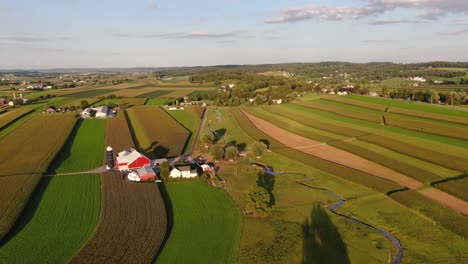 Aerial-turn-to-reveal-red-barn,-blue-silo,-vast-farmland-fields-in-Lancaster-County,-Pennsylvania-during-summer