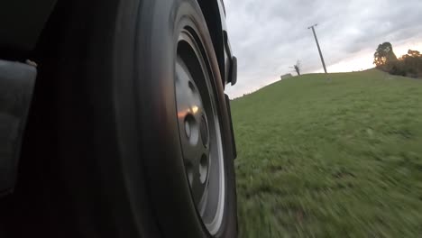 Close-up-Gopro-footage-of-4wd-back-wheel-driving-across-grassy-field-at-sunset