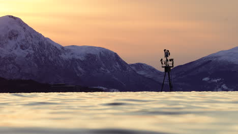 Navigation-mark-in-the-fjord-covered-with-cormorants-during-sunset