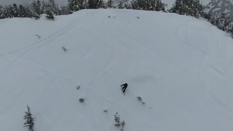 4K-drone-aerial-footage-of-a-snowboarder-riding-down-a-steep-hill-in-the-snowy-backcountry-of-the-Sierra-Nevada-mountains-in-Lake-Tahoe