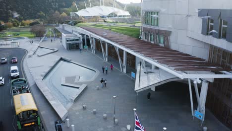 A-low-shot-above-the-road-in-front-of-the-Holyrood-Scottish-Parliament,-with-a-tourist-bus,-traffic-and-tourists