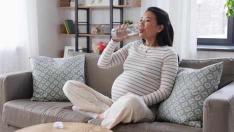 Mujer-Embarazada-Con-Agua-En-Botella-De-Vidrio-En-Casa.-Concepto-De-Embarazo,-Descanso,-Personas-Y-Expectativas.-Feliz-Sonriente-Mujer-Embarazada-Asiática-Sentada-En-Un-Sofá-En-Casa-Y-Bebiendo-Agua-De-Una-Botella-De-Vidrio-Reutilizable.