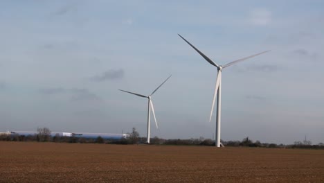 A-pair-of-slowly-spinning-wind-turbines-in-the-middle-of-a-brown-field