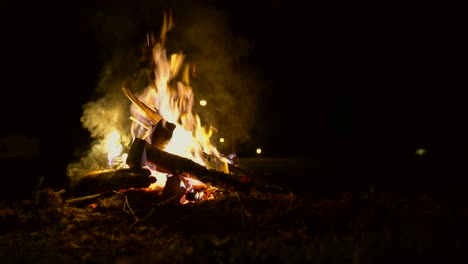 Toma-Estática-De-Una-Fogata-Por-La-Noche-Mientras-Un-Trozo-De-Madera-Se-Quema-Lentamente-Y-Cae-Al-Fuego.