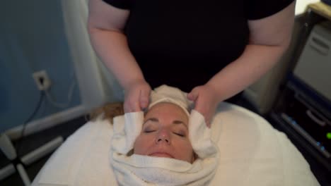 Massage-therapist-wraps-a-hot-wet-towel-around-a-beautiful-mature-woman’s-face-as-she-prepares-for-a-facial