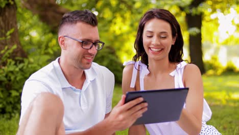 Happy-Couple-with-Tablet-Pc-at-Summer-Park.leisure-and-people-concept--happy-couple-with-tablet-pc-computer-at-summer-park