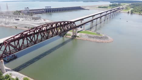 Flight-towards-railroad-and-vehicular-bridge-over-water-with-dam-in-background,-Kentucky,-forward-aerial-descend