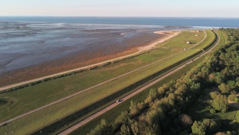 Vista-Aérea-Del-Tráfico-En-La-Carretera-Costera-Entre-El-Bosque-Y-La-Playa-Del-Mar-Del-Norte-Durante-La-Marea-Baja,-Alemania