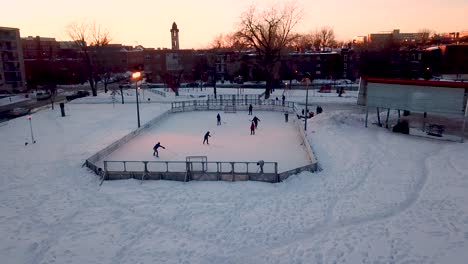 Un-Dron-Vuela-Alrededor-De-Jugadores-De-Hockey-En-Una-Pista-Al-Aire-Libre-Al-Anochecer-En-Montreal,-Quebec,-Canadá