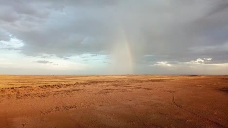 Drohnenaufnahme-Eines-Regenbogens-In-Der-Ferne-Auf-Einer-Sehr-Trockenen-Namibischen-Schaffarm