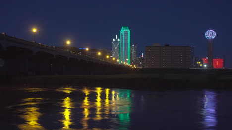 4k-–-Zeitraffer-–-Skyline-Von-Dallas-Bei-Nacht-Mit-Dem-Trinity-River-Im-Vordergrund-Und-Rauschendem-Wasser-Im-Vordergrund