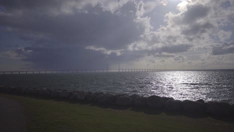 Storm-clouds-and-bright-midday-sun-over-Öresund-strait-Bridge-seen-from-Malmo-side-Sweden,-handheld