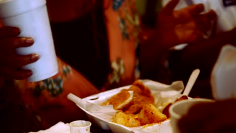 Black-woman-sits-down-with-drink-in-her-hand-to-continue-eating-a-seafood-feast-while-out-with-her-family