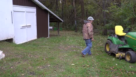 A-man-storing-his-lawn-and-garden-tractor-in-the-barn-with-his-dog-running-around