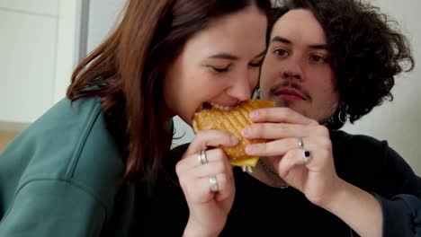 A-brunette-girl-in-a-green-jacket-bites-a-sandwich-that-her-boyfriend-is-holding-in-his-hands-who-wanted-to-eat-the-sandwich-himself-at-home