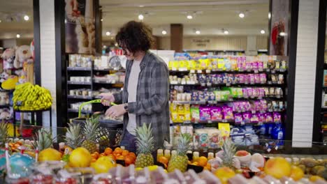 A-brunette-guy-with-curly-hair-in-a-plaid-shirt-chooses-fruits-in-a-supermarket-while-shopping-in-a-grocery-store