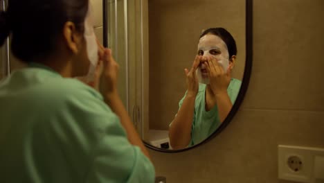 A-confident-brunette-girl-with-brown-skin-in-a-Green-nightie-makes-a-special-mask-applied-to-her-face-in-the-evening-in-a-modern-apartment-in-the-bathroom-before-going-to-bed