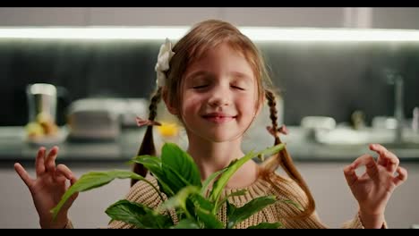 Portrait-Close-up-of-a-happy-little-calm-brown-haired-girl-with-a-braided-hairstyle-sits-in-the-lotus-position-and-practices-Zen-and-meditation-with-a-houseplant-in-a-modern-kitchen-in-the-evening