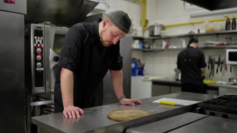 Tired-male-professional-chef-in-a-black-uniform-takes-off-his-work-cap-and-tries-to-relax-during-a-hard-day-of-work-in-the-kitchen-of-a-restaurant