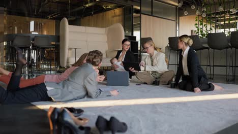 Zoom-in-confident-brunette-girl-in-business-clothes-breastfeeds-her-little-baby-during-a-meeting-on-the-floor-on-the-carpet-in-a-modern-office