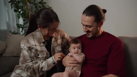 Close-up-of-happy-parents-a-young-girl-and-a-man-in-a-red-t-shirt-holding-their-little-baby-daughter-in-their-arms-and-playing-with-her-during-their-Happy-time-at-home-together-as-a-family-in-a-modern-apartment