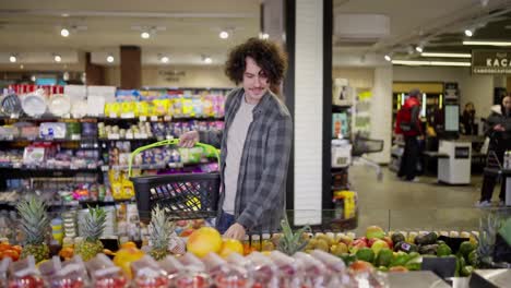 Happy-guy-with-basket-chooses-citrus-fruits-in-supermarket-while-shopping.-Guy-in-a-plaid-shirt-with-curly-hair-in-a-grocery-store