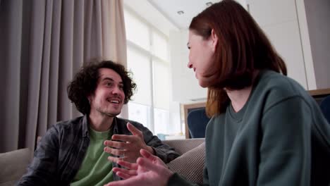 A-happy-brunette-guy-with-curly-hair-in-a-checkered-shirt-is-actively-communicating-with-his-brunette-girlfriend-while-sitting-on-the-couch-at-home