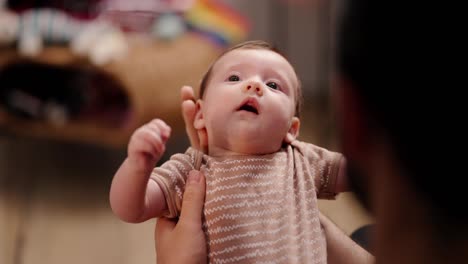 Top-view-of-a-little-baby-girl-in-light-brown-with-her-young-brunette-father-in-a-modern-apartment.-Over-the-shoulder-of-a-happy-young-brunette-man-holding-a-little-baby-girl-in-his-arms